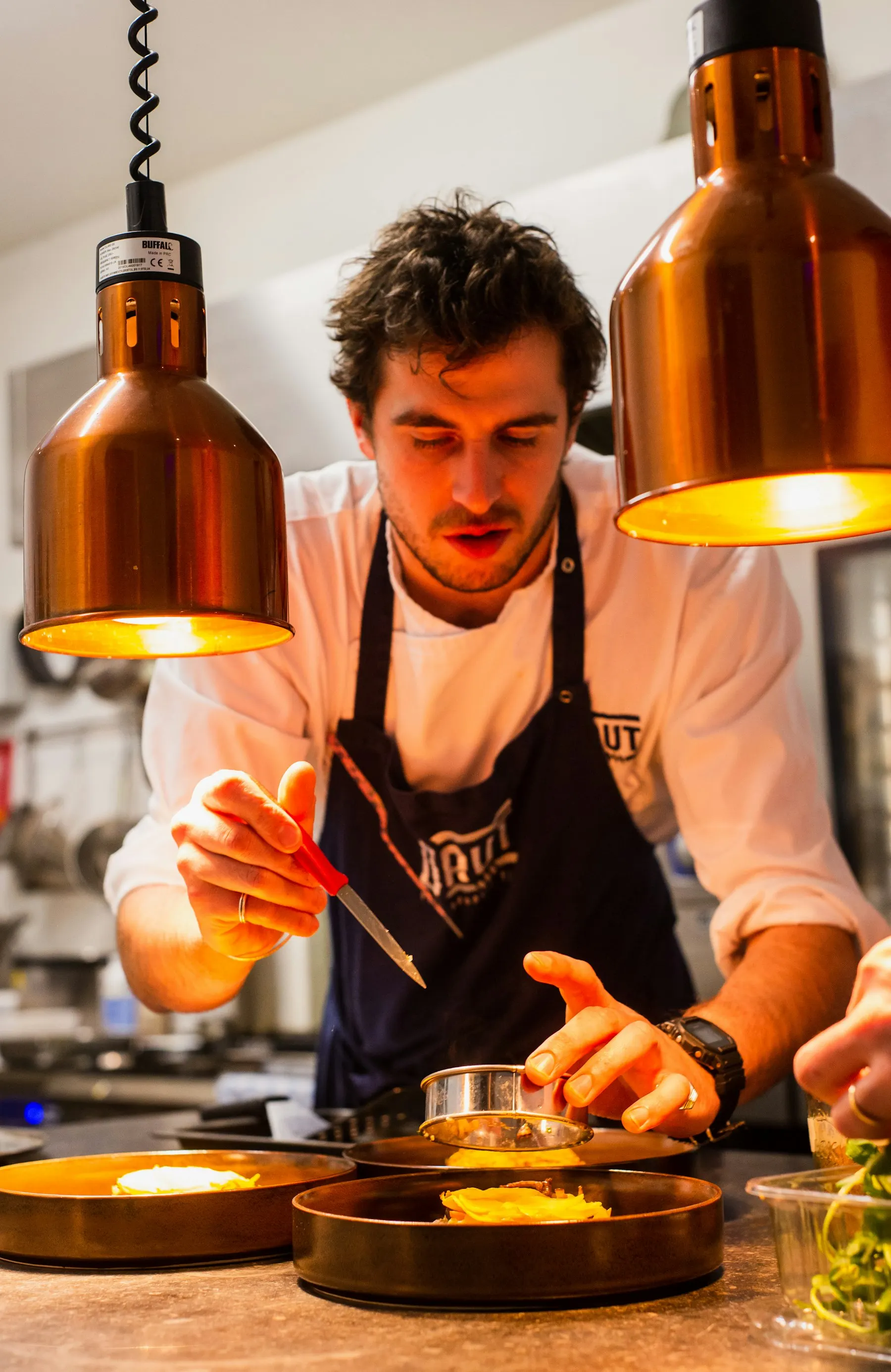 Chef plating a dish under warm heat lamps